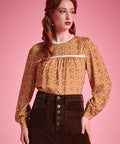 Woman wearing brown floral prairie blouse with lace trim and long sleeves against pink background