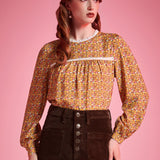 Woman wearing brown floral prairie blouse with lace trim and long sleeves against pink background