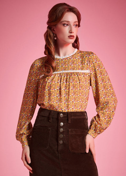Woman wearing brown floral prairie blouse with lace trim and long sleeves against pink background