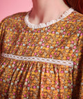 Close-up of brown ditsy floral blouse showing white ruffled neckline, lace yoke trim and gathered front