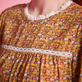 Close-up of brown ditsy floral blouse showing white ruffled neckline, lace yoke trim and gathered front