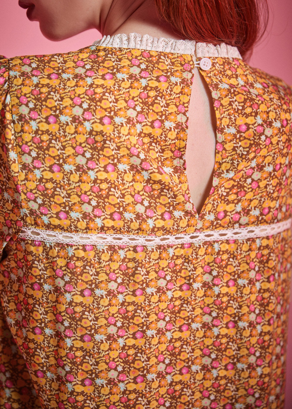 Close-up back view of brown floral blouse showing button keyhole closure and white lace trim
