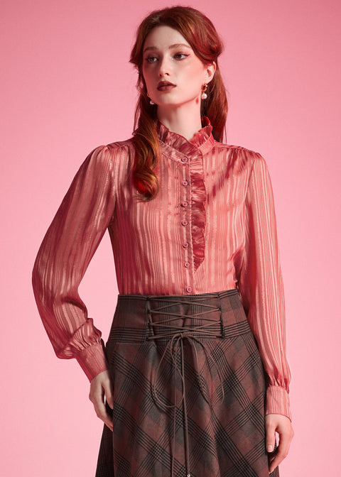 Woman wearing dusty rose ruffle button-front blouse tucked into a brown plaid corset-waist skirt against a pink background