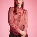 Woman wearing vintage-inspired dusty rose ruffle blouse with shimmering stripes and long sleeves against a pink studio background