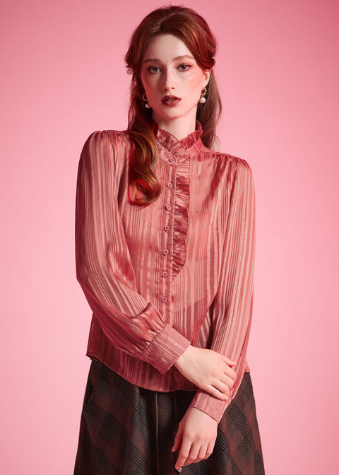 Woman wearing vintage-inspired dusty rose ruffle blouse with shimmering stripes and long sleeves against a pink studio background
