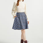 Woman wearing Poetry in Motion Blouse with high ruffle neck, long gathered sleeves and blue plaid skirt