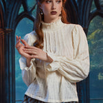 Woman wearing off white Victorian poet blouse with smocked high neck, pintucks and ruffle cuffs styled with a blue plaid skirt