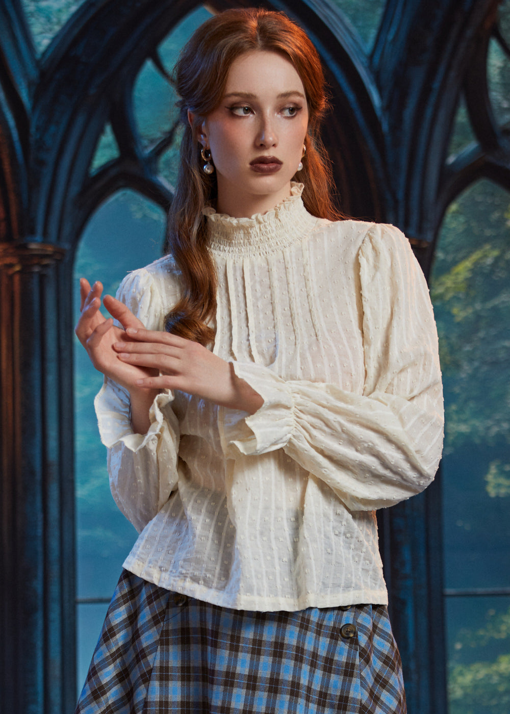 Woman wearing off white Victorian poet blouse with smocked high neck, pintucks and ruffle cuffs styled with a blue plaid skirt