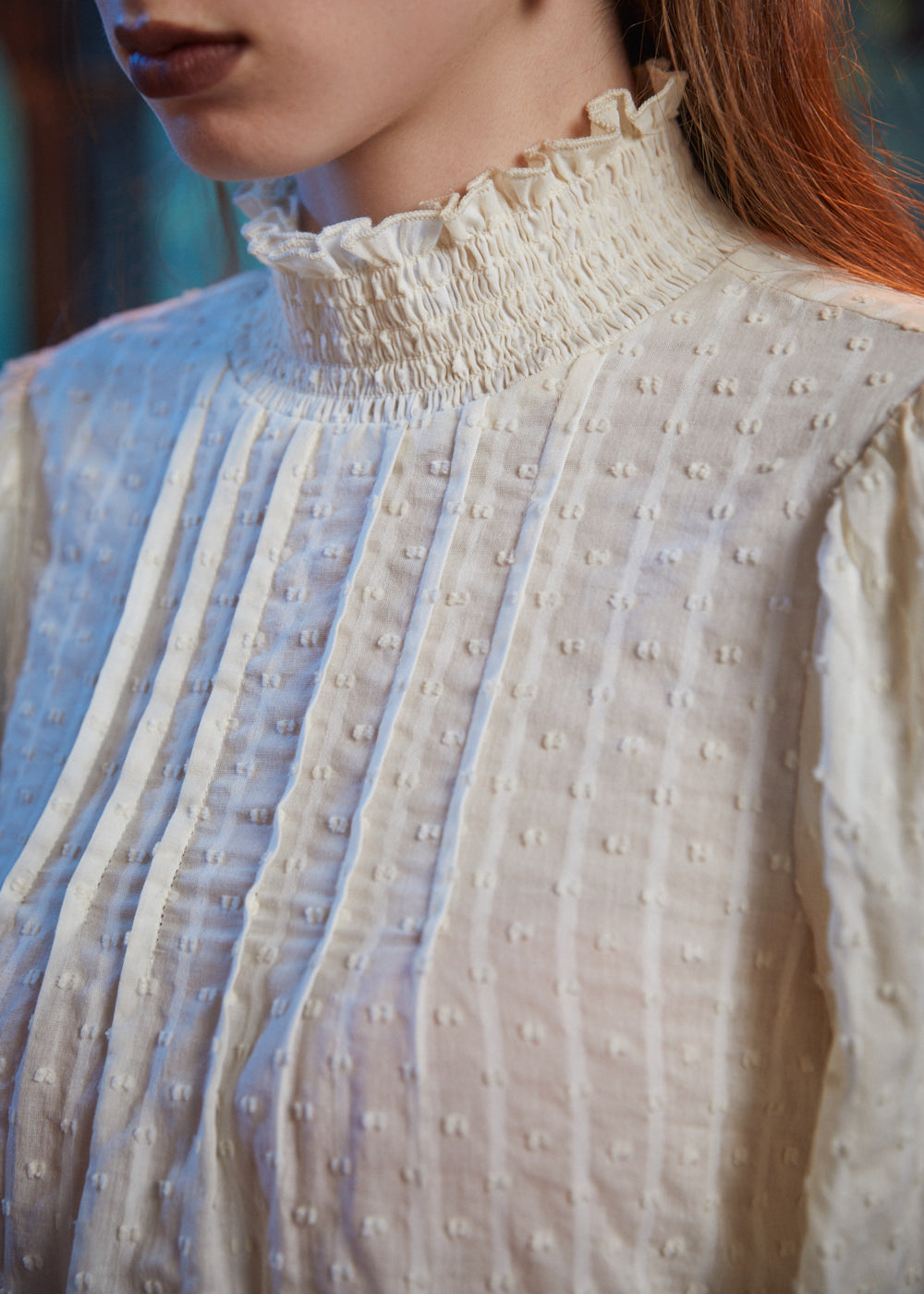 Close-up of cream color textured blouse showing smocked ruffle neckline, front pintucks and raised dobby weave