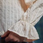 Close-up of cream dobby striped poet blouse sleeve showing elasticized wrist and flared ruffle cuff