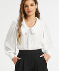 Front view of woman wearing ivory long sleeve blouse with polka dot necktie and black trousers