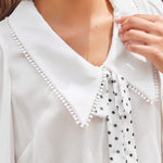 Close-up of ivory blouse with oversized pointed collar, pom-pom trim and black polka dot necktie