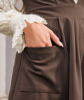 Woman showing the oversized front patch pocket on the brown Layer It On Me Jumper with pleated skirt.