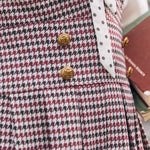 Close-up of burgundy houndstooth jumper dress with decorative gold-tone buttons