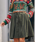 A woman wearing a festive crewneck sweater with a green base, red and white patterned trim, and brown squirrel illustrations, paired with an olive green button-front skirt and a brown braided belt.