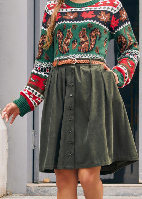 A woman wearing a festive crewneck sweater with a green base, red and white patterned trim, and brown squirrel illustrations, paired with an olive green button-front skirt and a brown braided belt.