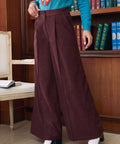 Woman wearing Mahogany Wine high waisted wide leg pants showing front pleats, center creases and button pocket details