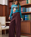Woman wearing Mahogany Wine corduroy wide leg pants styled with teal novelty cat sweater and black heels in library