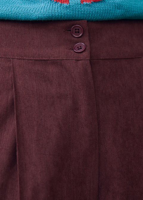 Close-up of Mahogany Wine corduroy pants showing double-button waistband, front pleat and textured fabric
