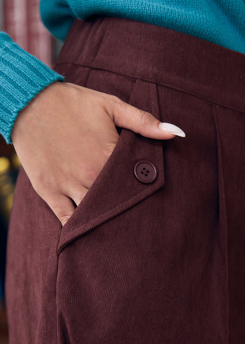 Close-up of woman wearing Mahogany Wine corduroy pants showing functional side pocket with button-tab detail