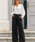 Woman wearing black high waisted wide leg pants with pleated front, white blouse and red heels