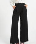 Woman wearing black pleated wide leg trousers with hands in pockets and red heels