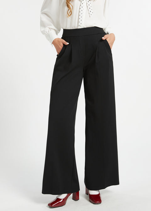 Woman wearing black pleated wide leg trousers with hands in pockets and red heels