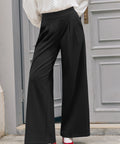 Woman wearing black pleated wide leg pants with high-rise waistband and full-length legs