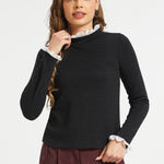 Woman wearing black lace trim mock neck top with long sleeves and burgundy trousers against white studio background