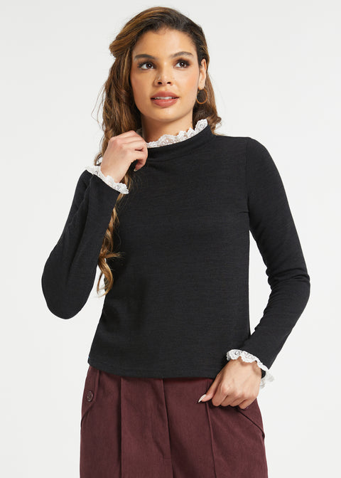 Woman wearing black lace trim mock neck top with long sleeves and burgundy trousers against white studio background