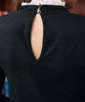 Close-up of black mock neck top with back keyhole and two button closures trimmed with white lace