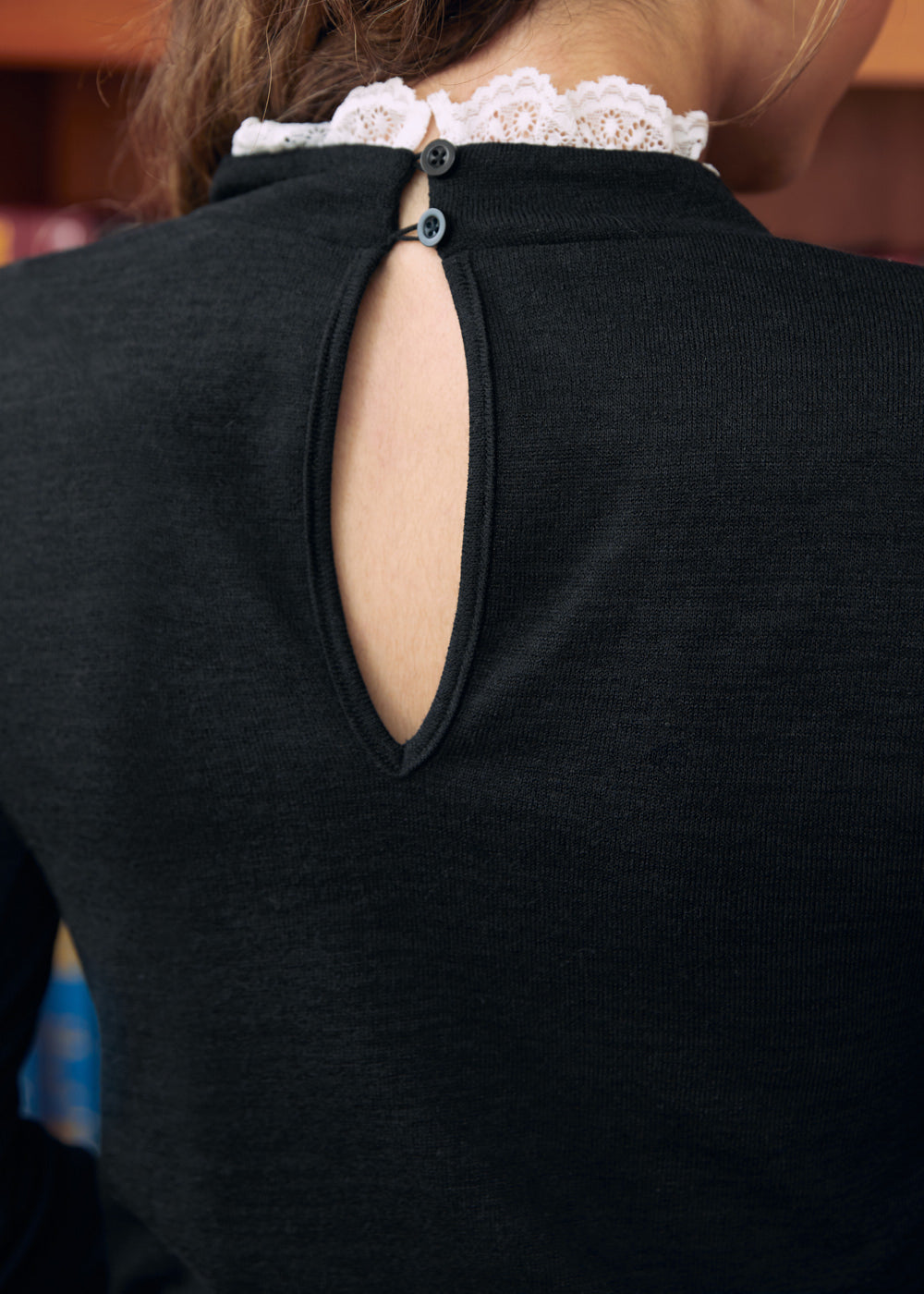 Close-up of black mock neck top with back keyhole and two button closures trimmed with white lace