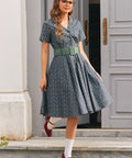 Full-length woman wearing blue floral belted shirt dress with side pockets, white socks and red Mary Jane shoes