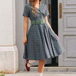 Full-length woman wearing blue floral belted shirt dress with side pockets, white socks and red Mary Jane shoes