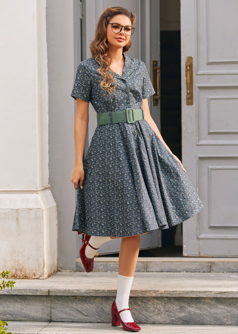 Full-length woman wearing blue floral belted shirt dress with side pockets, white socks and red Mary Jane shoes