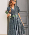 Woman holding books while wearing vintage-inspired blue floral shirt dress with sage belt and full knee-length skirt