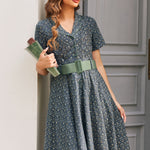 Woman holding books while wearing vintage-inspired blue floral shirt dress with sage belt and full knee-length skirt