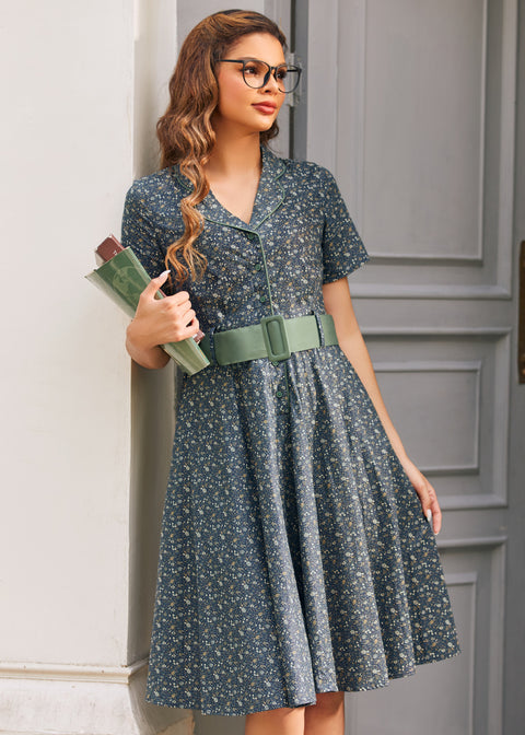 Woman holding books while wearing vintage-inspired blue floral shirt dress with sage belt and full knee-length skirt