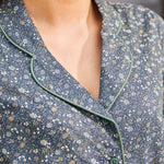 Close-up of woman wearing vintage-inspired blue floral dress showing notched collar, sage green piping and button front