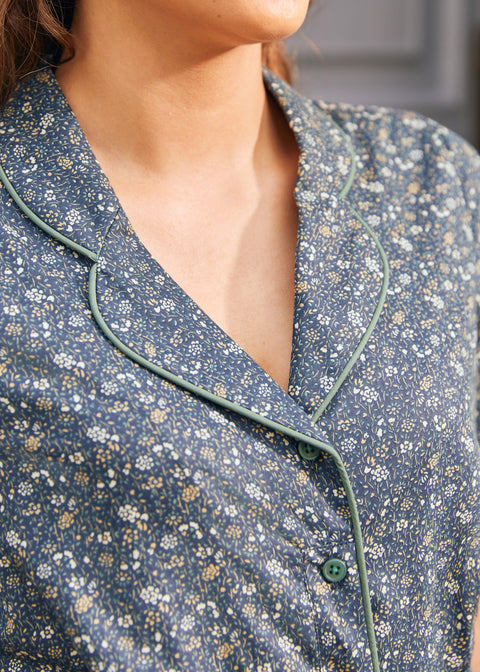 Close-up of woman wearing vintage-inspired blue floral dress showing notched collar, sage green piping and button front
