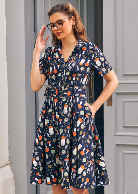 Woman wearing navy novelty mushroom print dress with short sleeves, button front bodice and side pockets