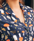 Close-up of a woman wearing a navy dress with a colorful mushroom print, showing the collar, button placket, and chest area.