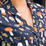 Close-up of a woman wearing a navy dress with a colorful mushroom print, showing the collar, button placket, and chest area.