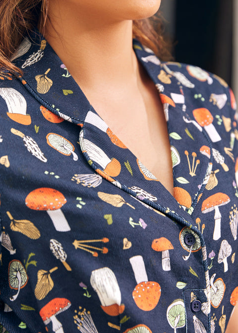Close-up of a woman wearing a navy dress with a colorful mushroom print, showing the collar, button placket, and chest area.