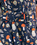 Close-up of a navy blue fabric shirtdress with an allover mushroom print in orange, white, beige, and green, featuring a matching fabric belt with a covered buckle.