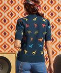 Woman wearing navy dinosaur short sleeve sweater and jeans, back view showing multicolor dinosaur motif