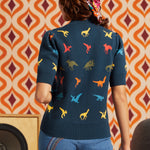 Woman wearing navy dinosaur short sleeve sweater and jeans, back view showing multicolor dinosaur motif