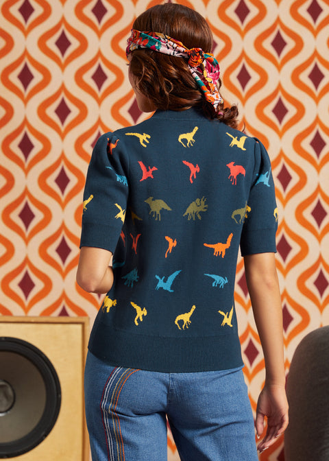 Woman wearing navy dinosaur short sleeve sweater and jeans, back view showing multicolor dinosaur motif