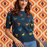 A woman wearing a navy blue sweater with a colorful dinosaur print, styled with a floral headband and blue jeans, set against a retro orange and brown patterned wall.