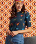 A woman wearing a navy blue short-sleeve top with a colorful dinosaur print, styled with a floral headband and blue jeans, set against a retro orange and brown patterned background.